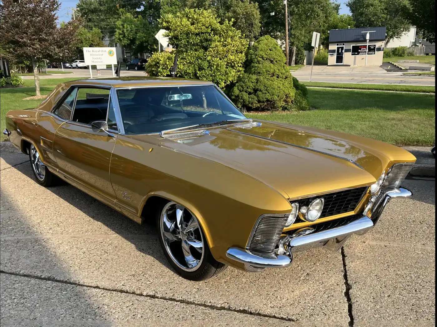 The unedited camera photo: a gold 1960s Buick Riviera parked on a suburban street in daylight.